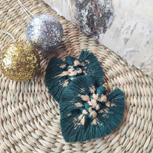 Load image into Gallery viewer, Gold Digger makramee-korvikset sävyssä Forest Green, kuvassa oikealla koivuhalko ja vasemmalla ylhäällä hopeinen ja kultainen joulupallo.