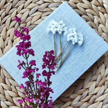 Load image into Gallery viewer, Kaksi valkoista makramee-klemmaria vaalean vihon päällä, etualalla violetteja kanervia.