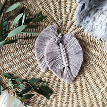 Load image into Gallery viewer, The Feather Girls macramé earrings in colour Sand, green eucalyptus leaves on the left side of the picture.