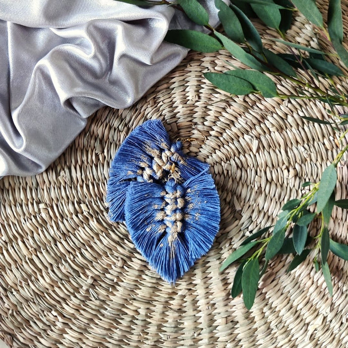 Gold Digger macramé earrings in colour Night Sky with gold paint splatters, green eucalyptus leaves on the right side of the picture.