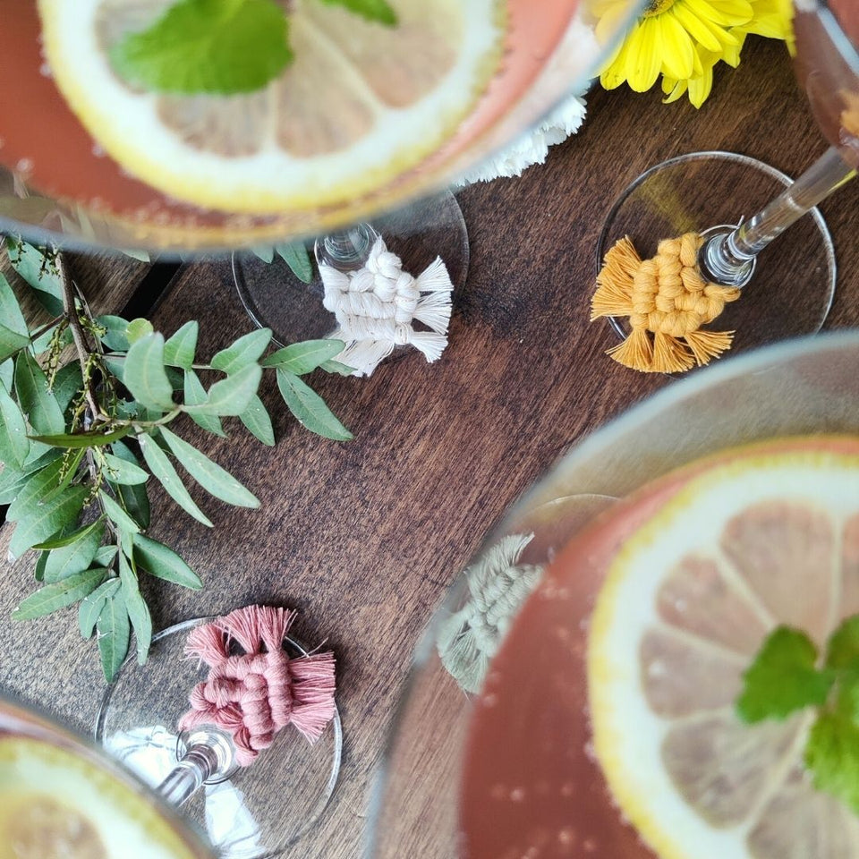 Four cocktail glasses with pink drink and lemon slices, with macramé Wineglass Charms in shade Garden Party on the stems.