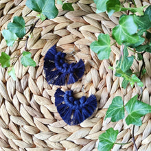 Load image into Gallery viewer, Sunburst macramé earrings in a shade Deep Navy, laying flat on a straw place mat, green leaves on the sides.
