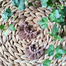 Load image into Gallery viewer, Sunburst macramé earrings in a shade Hot Cocoa, laying flat on a straw place mat, green leaves on the sides.
