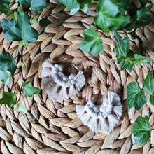 Load image into Gallery viewer, Sunburst macramé earrings in a shade Natural, laying flat on a straw place mat, green leaves on the sides.
