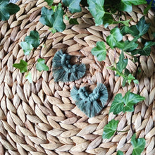 Load image into Gallery viewer, Sunburst macramé earrings in a shade Sage, laying flat on a straw place mat, green leaves on the sides.
