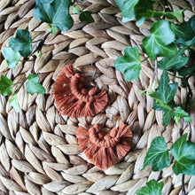 Load image into Gallery viewer, Sunburst macramé earrings in a shade Tumeric, laying flat on a straw place mat, green leaves on the sides.
