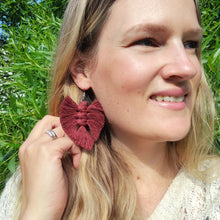 Load image into Gallery viewer, A model wearing The Feather Babies macramé earrings in colour chocolate, green leaves on the background.
