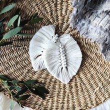Load image into Gallery viewer, The Feather Girls macramé earrings in colour Natural, green eucalyptus leaves on the left side of the picture.
