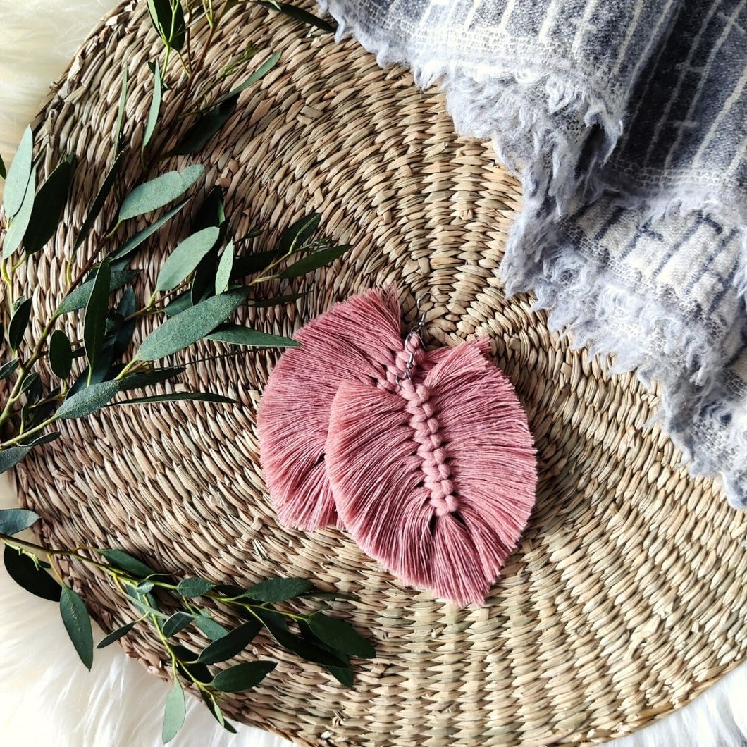 The Feather Girls macramé earrings in colour Vintage Rose, green eucalyptus leaves on the left side of the picture.
