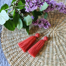 Load image into Gallery viewer, Macramé tassel earrings Pillow Talk in shade Brick laying flat on a straw place mat, lilacs on the side.

