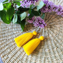 Load image into Gallery viewer, Macramé tassel earrings Pillow Talk in shade Sunshine laying flat on a straw place mat, lilacs on the side.
