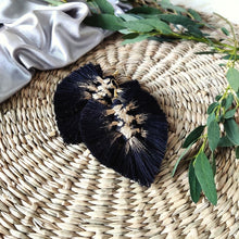 Load image into Gallery viewer, Gold Digger macramé earrings in colour Black with gold paint splatters, green eucalyptus leaves on the right side of the picture.
