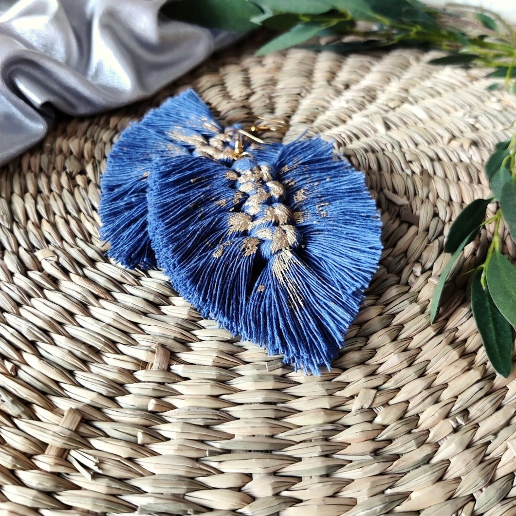 Gold Digger macramé earrings in colour Night Sky with gold paint splatters, green eucalyptus leaves on the right side of the picture.