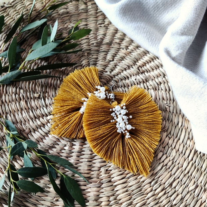 Uptown Pearl macramé earrings in colour Ocra, green eucalyptus leaves on the left side of the picture.